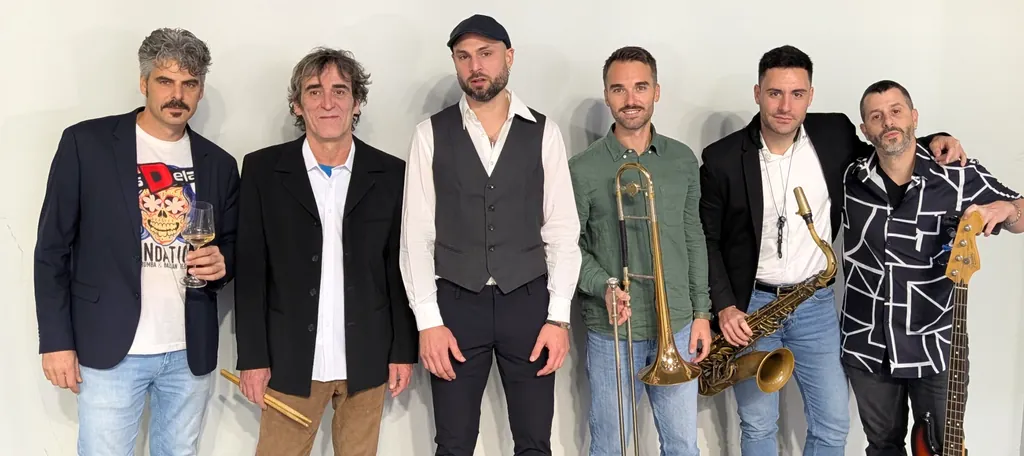 Foto de grup dels sis músics d'Els Delai davant d'una paret blanca, amb les baquetes, el trombó, el saxo i el baix